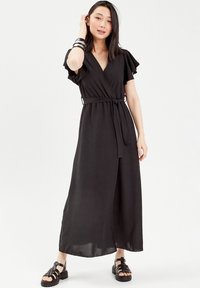 Robe noire à manches courtes volantes, taille ceinturée et jupe longue. Fabriquée en tissu léger avec une texture douce.