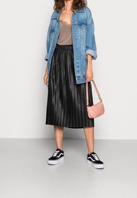 Giubbino in denim, top beige, gonna midi plissettata nera, borsa rosa e sneakers nere con suola bianca. Texture lisce e design stratificato.