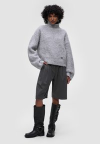 Šedý chlupatý pletený svetr s vysokým límcem, kombinovaný se šedými skládacími šortkami a černými vysokými botami s přezkou.