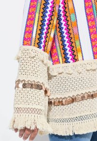 Maglione all'uncinetto con motivo a strisce colorate; maniche beige con frange adornate da dettagli di monetine e lavorazione a maglia testurizzata.