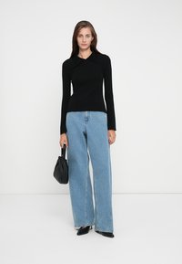Svart langermet topp med spiss krage, kombinert med høyt liv lys blå bredbein jeans. Bærer en svart veske og har på seg svarte sko.