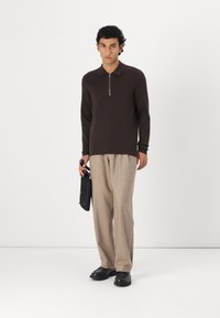 Brown zippered sweater, beige textured pants, and black shoes. The outfit features a relaxed fit with a classic collar design.