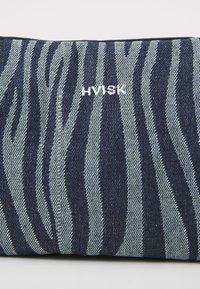 Denim clutchväska med ett mönster av zebraränder i mörkblått och ljust blått, accentuerad med en vit "HVISK"-logotyp. Slät textur med en strukturerad form.