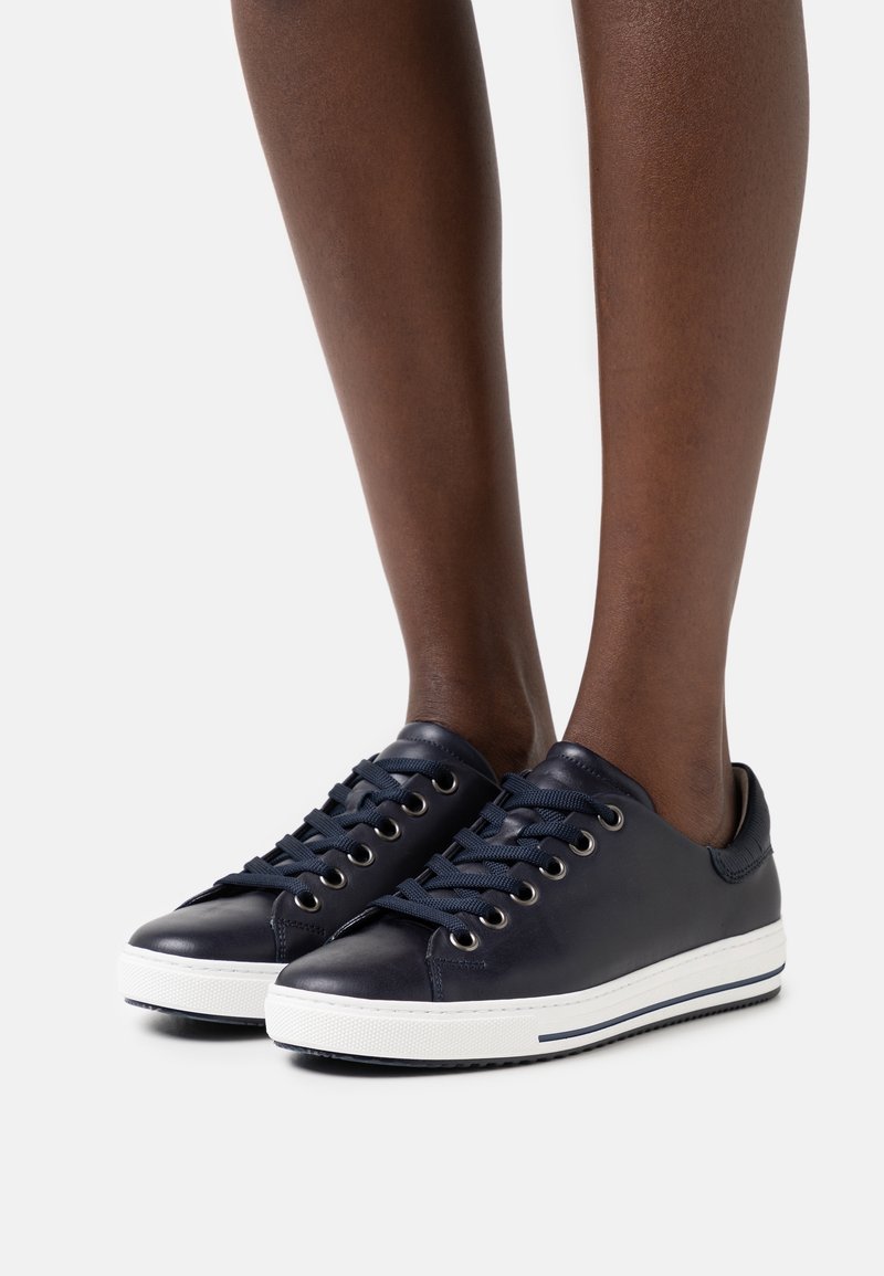 Sneakers in pelle navy con suola in gomma bianca, punta tonda e occhielli in metallo. Presentano lacci piatti navy e un design minimalista.