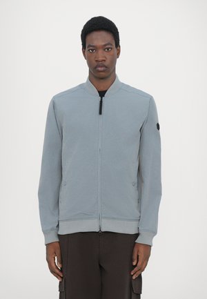 Gray zippered bomber jacket with ribbed collar and cuffs, side pockets, and a black logo patch on the left sleeve. Made from lightweight fabric.
