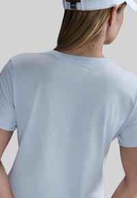 Maglietta di cotone leggera di colore azzurro, con maniche corte e colletto a girocollo, caratterizzata da una texture liscia e cuciture pulite, vista di spalle.