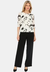 Biała bluzka z czarnym kwiatowym wzorem, z rękawami do trzech czwarte, w zestawie z czarnymi spodniami o szerokich nogawkach i czarnymi wysokimi obcasami. Gładka tekstura materiału.