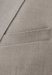 Hellbraunes Sakkorevers mit einer Paspeltasche auf der Brust und feiner strukturierter Stoff.