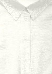 Witte overhem shirt met een gestructureerd oppervlak, voorzien van een klassieke kraag en vijf doorzichtige plastic knopen langs de voorkant.