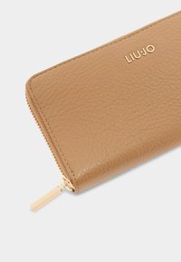 Portafoglio in pelle color tan con finitura testurizzata, dotato di una cerniera dorata e dettagli con logo. Forma rettangolare compatta.