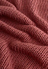 Plaid en tricot de couleur rose foncé, présentant des vagues texturées et des motifs en côtes avec un fil épais et proéminent pour une apparence chaleureuse.