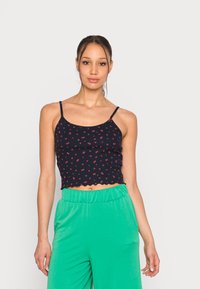 Top cropped azul-marinho com pequeno padrão floral vermelho, bainha em forma de ondas e alças finas ajustáveis, combinado com calças verdes largas.