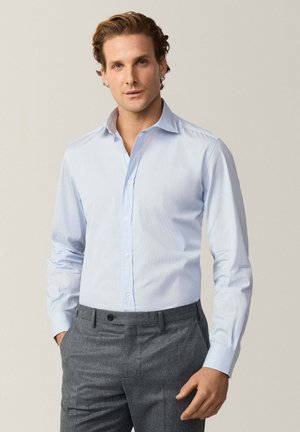 Camisa de vestir de manga larga en azul claro con cuello button-down y tejido liso. Combinada con pantalones grises con frente plano y cierre de botón.