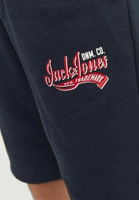Tamsiai mėlynos medvilninės šortai su raudonu ir baltu „Jack & Jones“ logotipu, išsiuvinėtu šone, su lygiu paviršiumi ir prigludusia forma.