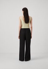 Light green, ribbed tank top with a deep V-back paired with black, pleated wide-leg pants. Smooth textures and relaxed fit.