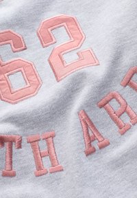 Harmaa collegepaita, jossa on vaaleanpunaiset kirjailut numerolla "62" ja tekstillä "SOUTH" samassa värissä. Materiaali on pehmeä ja teksturoidun tuntuinen.