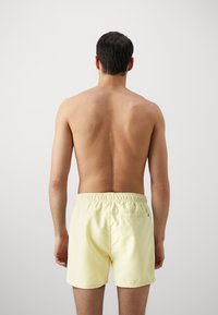 Shorts de bain pour hommes jaunes avec une taille élastique, en tissu doux, et une poche arrière. Le design est simple et sans embellissement.