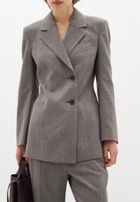 Šedý herringbone blazer s špičatými klopami a dvěma předními knoflíky, spárovaný s ladícími kalhotami na míru. Hladká textura, strukturovaný střih.
