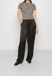 Svarta satinbredbenbyxor med dragsko i midjan, tillsammans med en kortärmad topp i svart och beige randig design, med texturerat tyg.