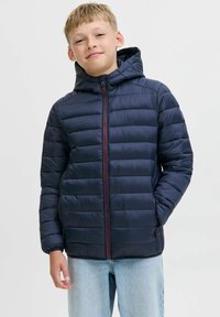 Marinblå puffjacka med dragkedja framtill, huva och horisontella quiltade paneler; har röd dragkedja och sidofickor. Bärs över ljusa jeans.