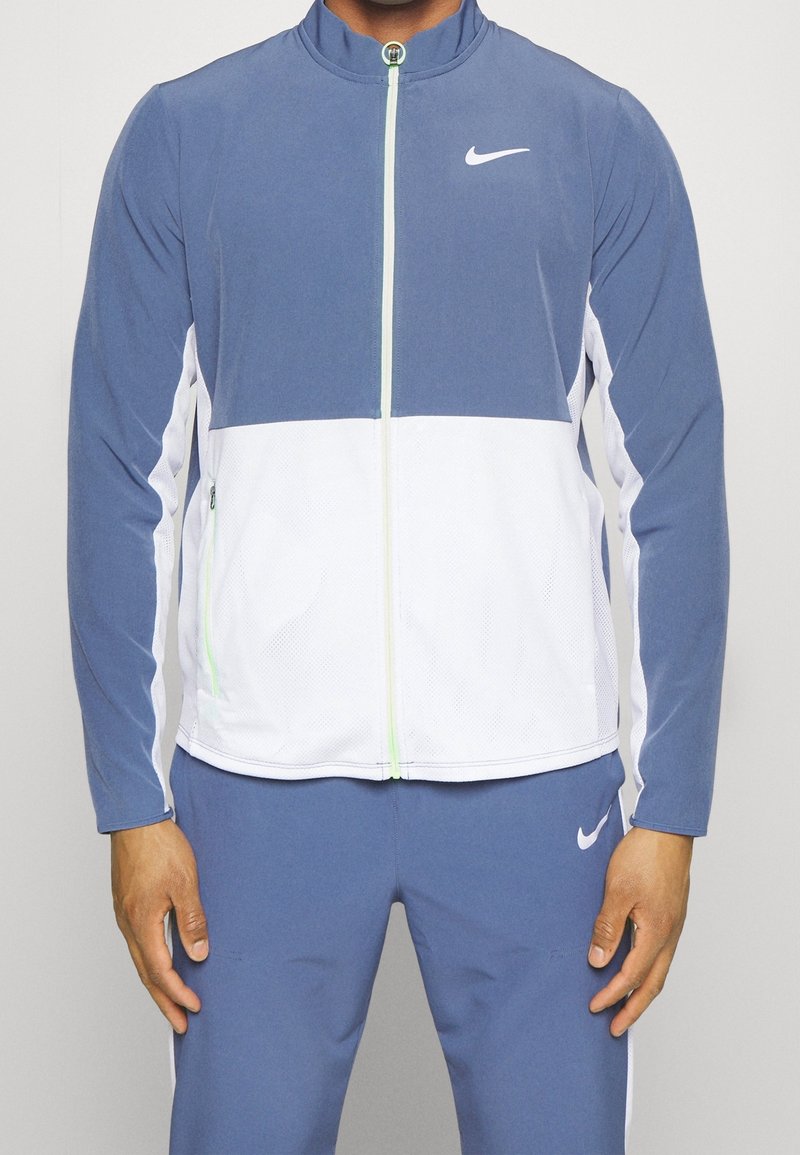 Nike jacket in blue and white, featuring a zip-front design, stand collar, and textured mesh accents. Smooth fabric with logo detail.