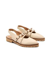 Zapatos slingback beige con punta afilada, correa decorativa con tachuelas metálicas y suelas de goma texturizadas para mayor agarre.