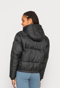 Svart dunjakke med hette, quiltet design, elastiske mansjetter og hem. Materialet er blankt og glatt, og gir varme og komfort.