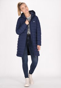 Marineblauwe gewatteerde jas met een capuchon, voorzien van een rits aan de voorkant, zijzakken en elastische manchetten, gecombineerd met een gestreept shirt en jeans.