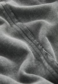 Gros plan d'un tissu gris montrant des coutures détaillées et un tissage texturé avec des plis doux et des ombres.