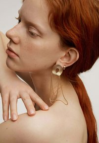 Pendientes de metal dorado con un diseño en espiral y cadenas colgantes. La textura es suave, y la forma es geométrica y fluida.