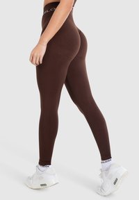 Leggings marroni realizzati in tessuto elasticizzato, con una vita alta e una trama liscia, abbinati a scarpe da ginnastica bianche.
