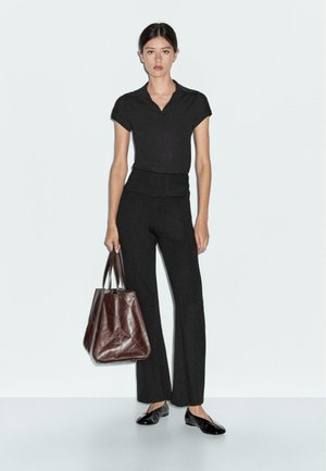Black polo top paired with black flared trousers. The model carries a brown leather tote bag with a structured, geometric design.