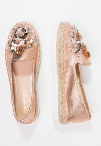 Espadrillas color oro rosa con decorazioni floreali e strass, tessuto metallizzato e suola in juta testurizzata. Design piatto, stile slip-on.