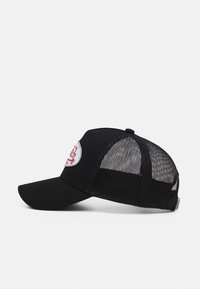 Zwarte trucker pet met een mesh achterkant, gebogen rand en een ronde geborduurde patch met rode details aan de voorkant.