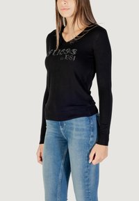Pullover nero a maniche lunghe con la scritta "Guess est. 1981" in dettaglio scintillante sul petto, realizzato in tessuto morbido e leggero.