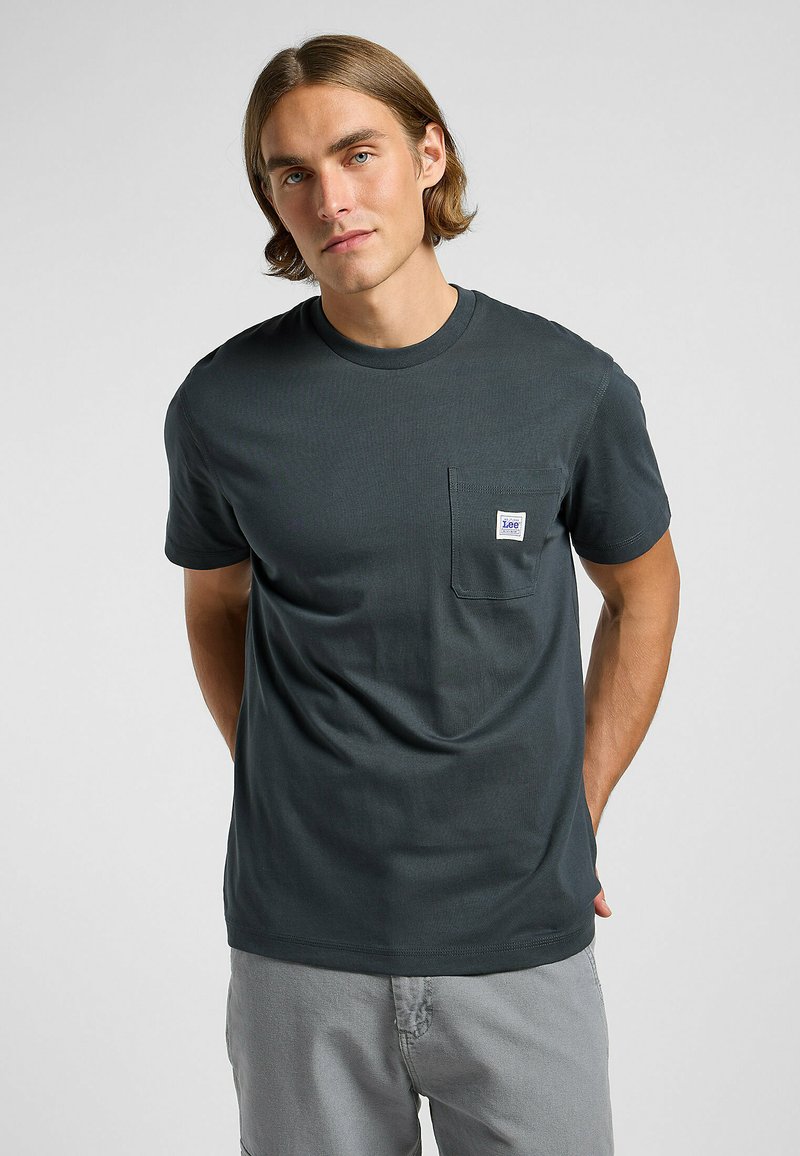 T-shirt grigio scuro a maniche corte realizzato in cotone, con taschino frontale dotato di una piccola etichetta di marca. Tessuto liscia e design aderente.