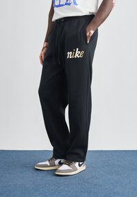 Čierne tepláky z bavlny s elastickým pásom, bočnými vreckami a zlatým logom "nike" na ľavom stehne.