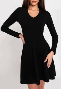 Robe noire ajustée à manches longues avec un col en V, jupe évasée et texture lisse. Design simple sans motifs ni détails visibles de quincaillerie.