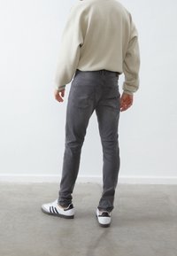 Jeans grises de mezclilla, diseño ajustado, bolsillos traseros visibles. Combinados con zapatillas blancas con rayas y acentos negros.