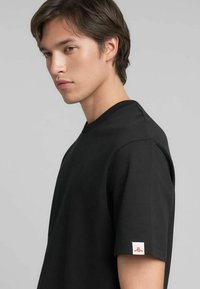 T-shirt nera con scollo a girocollo, realizzata in cotone, con maniche corte, tessuto strutturato e piccolo dettaglio logo sulla manica.