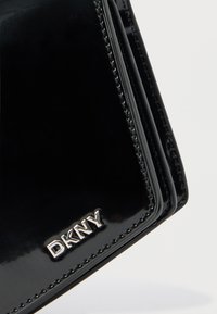 Fekete patentbőr pénztárca dombornyomott DKNY logóval. Karcsú, fényes textúrával és az éleknél látható varrással rendelkezik.