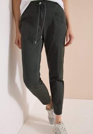 Pantalon noir slim-fit avec poches à l’avant et taille à cordon, porté avec des baskets blanches, présenté de la taille aux pieds sur un fond neutre.