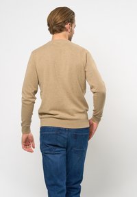 Lichtbeige gebreide trui met ronde hals, inzetmouwen en geribde manchetten, gecombineerd met blauwe denim jeans. Zachte textuur.