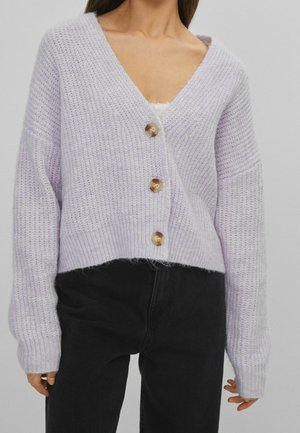 Lila gebreide cardigan met V-hals, vier grote knopen, cropped ontwerp en wijde mouwen, gecombineerd met zwarte high-waisted broek.