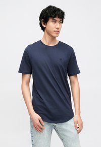 Mörkblå t-shirt i bomull med korta ärmar, rund halsringning och diskret logotypdetalj på bröstet. Matchas med ljusblå jeans i denim.