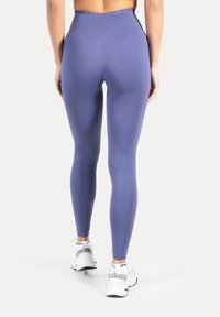 Leggings violets taille haute avec une texture lisse et une coupe ajustée, assortis à des chaussures de sport blanches.
