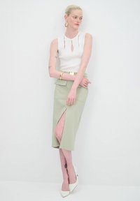 Weißes geripptes Tanktop mit Schlüsselloch-Design, kombiniert mit einem knielangen, hellgrünen Rock mit seitlichem Schlitz. Die Modells trägt weiße High Heels.