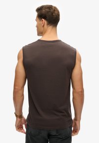 Camiseta sin mangas marrón hecha de algodón, con un cuello redondeado y un corte holgado. La parte trasera presenta una textura suave sin adornos.