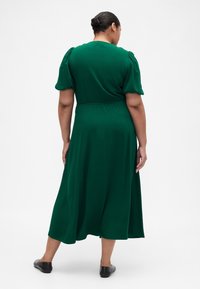 Roheline keskmise pikkusega kleit puffy varrukate, fitted vöökoha ja voolava seelikuga. Sile kangas ja peen tekstuur rõhutavad disaini.