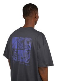 Mężczyzna z krótkimi włosami i kolczykiem w kształcie koła ubrany w ciemny, oversize'owy T-shirt z niebieskim abstrakcyjnym wzorem siatki na plecach.